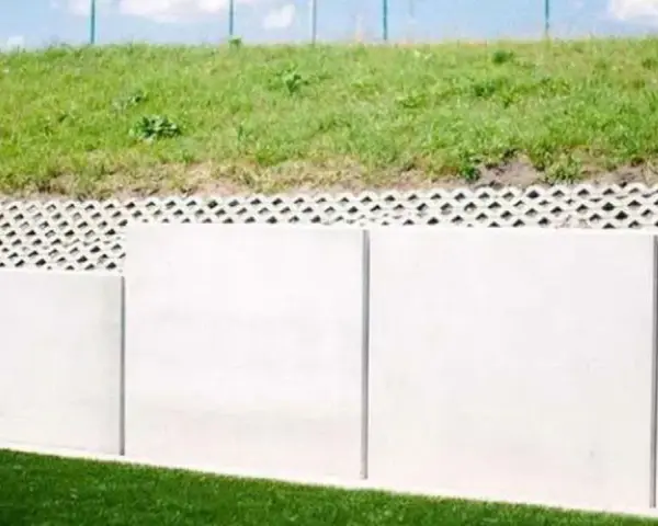 Betonowy mur oporowy z ażurową warstwą i zieloną skarpą.