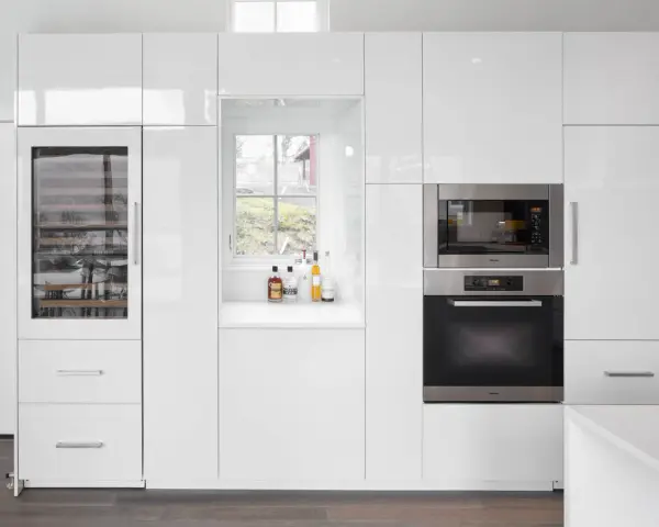 Cucina moderna bianca con elettrodomestici integrati e una porta finestra che offre una vista sul verde.