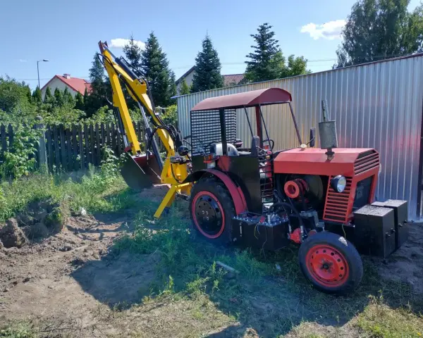 Czerwony traktor C-330 z zamontowaną żółtą koparką, gotowy do pracy w ogrodzie.