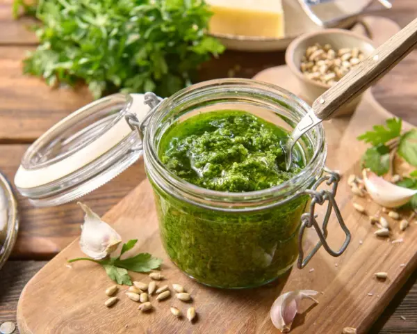 Słoik domowego pesto z pietruszki, z czosnkiem, nasionami słonecznika i serem w tle. Idealne do makaronu lub na grzanki.