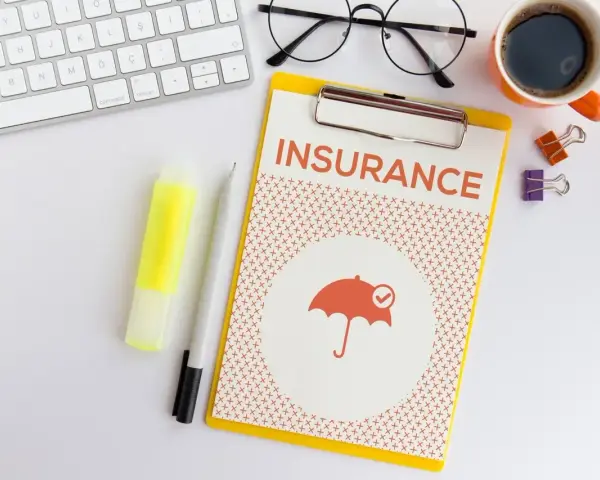 Dokument "Insurance" z parasolką, klawiatura, okulary, kawa. Planowanie ubezpieczenia zdrowotnego bez pracy.