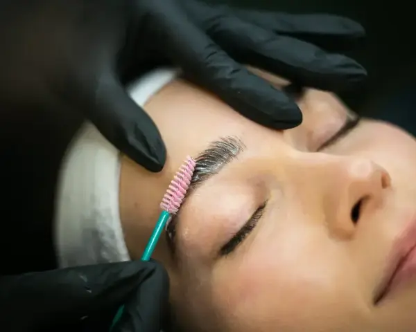 Stylist w czarnych rękawiczkach aplikuje produkt do laminacji brwi. Proces ten jest szybki i efektywny.