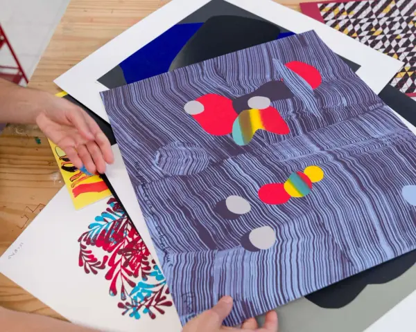Manos revisando impresiones de arte abstracto, con vibrantes colores y patrones. El material serigrafia resalta en cada detalle.