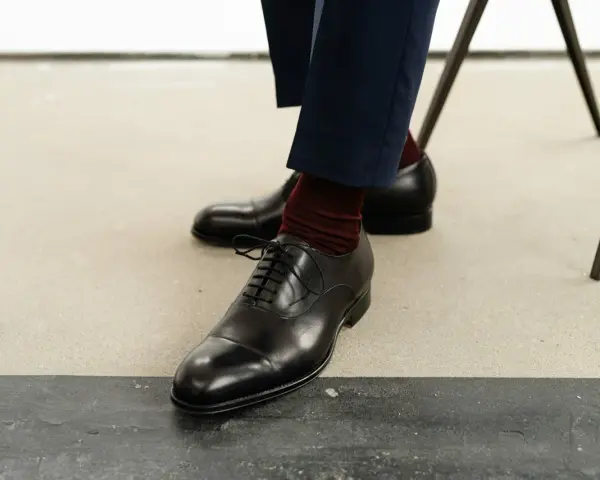 Eleganckie czarne buty męskie, rozmiar buta 50, z bordowymi skarpetkami i granatowymi spodniami.
