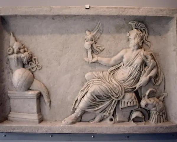 A marble relief depicting a seated figure, possibly a goddess, holding a winged victory. This scene reflects the rich tapestry of Roman paganism, with symbolic offerings and divine representation.