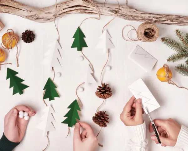 Kinder basteln Weihnachtsgeschenke: Papierbäume, Zapfen und Orangen werden zu einer festlichen Girlande.