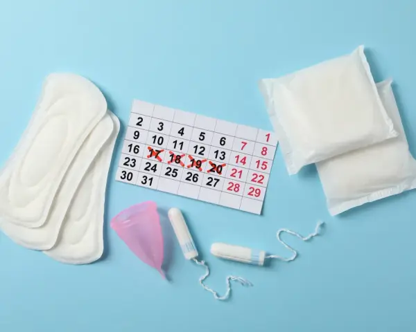 Kalender mit markierten Tagen, Binden, Tampons und Menstruationstasse. Fragen zu Zwischenblutung trotz Pille schwanger?