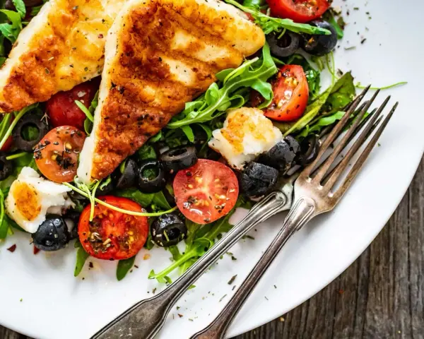 Pyszna sałatka z grillowanym halloumi, pomidorkami koktajlowymi i czarnymi oliwkami na talerzu.