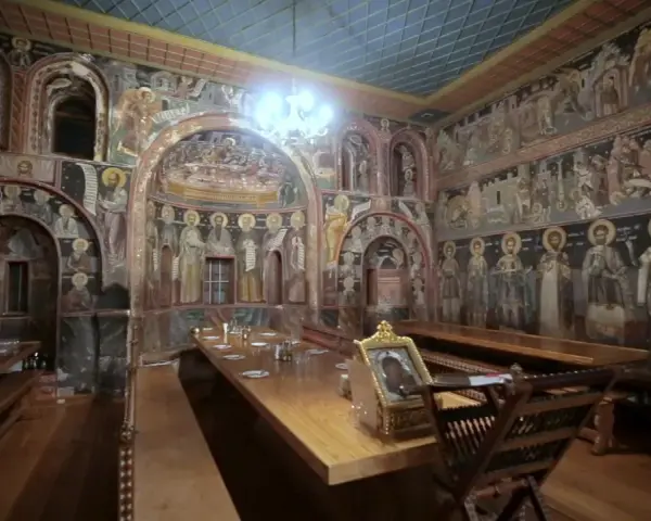 Inside Mount Athos, a refectory is adorned with ancient frescoes depicting religious scenes and figures.