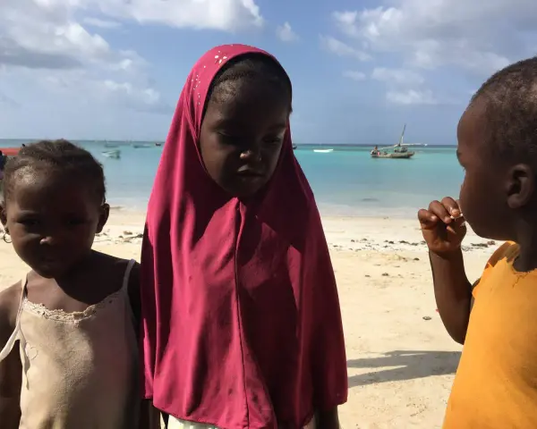 Dzieci na plaży, w tle turkusowe morze i łodzie. To obrazek z życia na Zanzibarze.