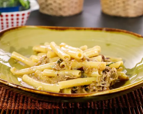 Piatto di ziti alla genovese, pasta condita con un ricco ragù di carne, servita in una ciotola verde.