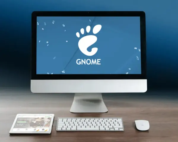 Komputer z logo GNOME, tablet i klawiatura na drewnianym biurku.