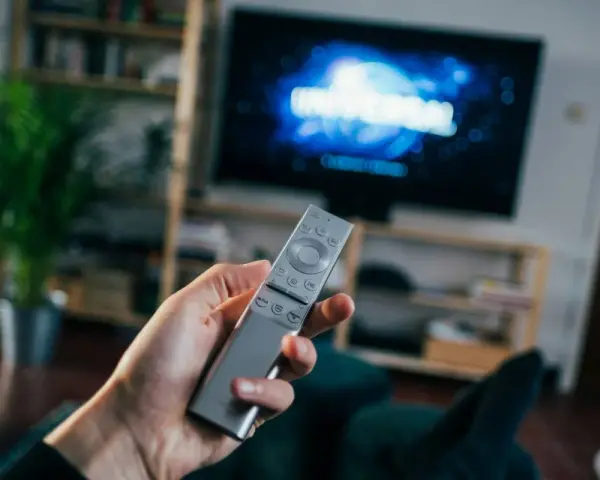 Dłoń trzymająca srebrny pilot do telewizora, na ekranie logo Universal.