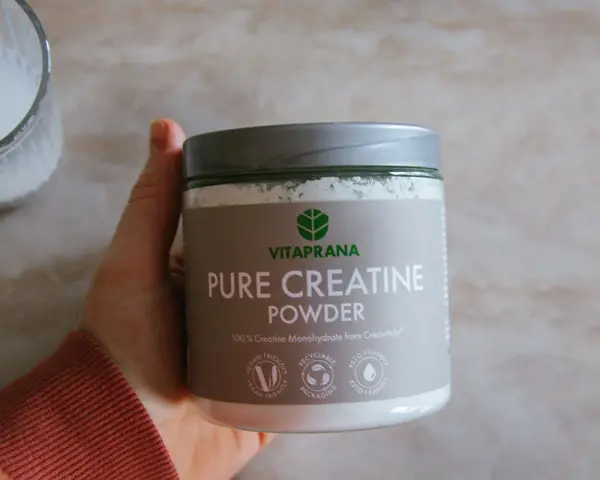 En hand håller en burk med Vitaprana Pure Creatine Powder. Kan vara ett komplement för den som vill ha **kreatin viktnedgång**.