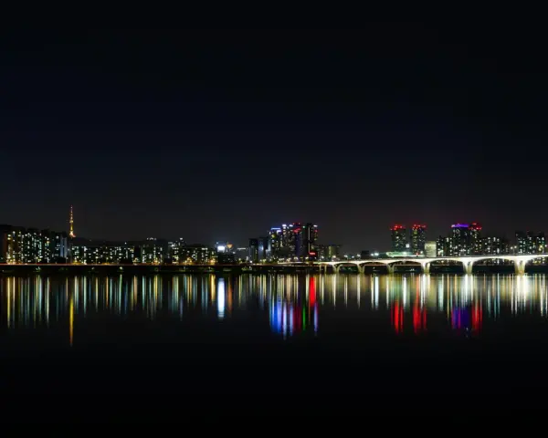 Nocny widok na Seul z rzeką Han, mostem i wieżą Namsan. Światła miasta odbijają się w wodzie, tworząc magiczny krajobraz. Itaewon tętni życiem.