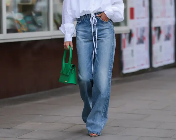 Mujer con camisa blanca y pantalones vaqueros anchos, a la altura de la cintura, con un bolso verde brillante.