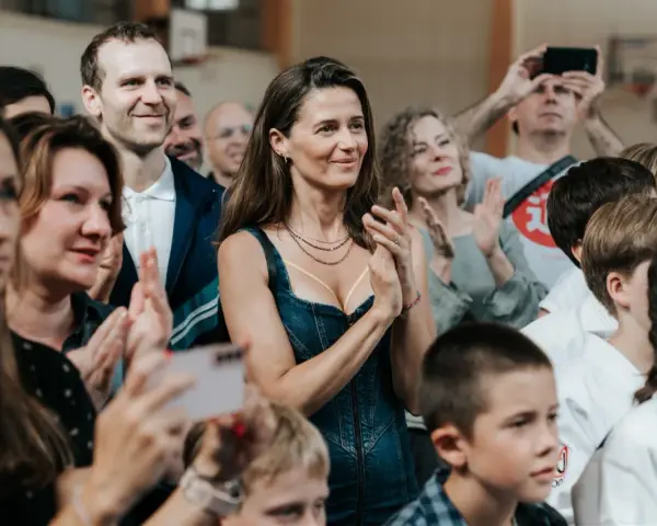 Agnieszka Grochowska z uśmiechem klaszcze, otoczona ludźmi na widowni.