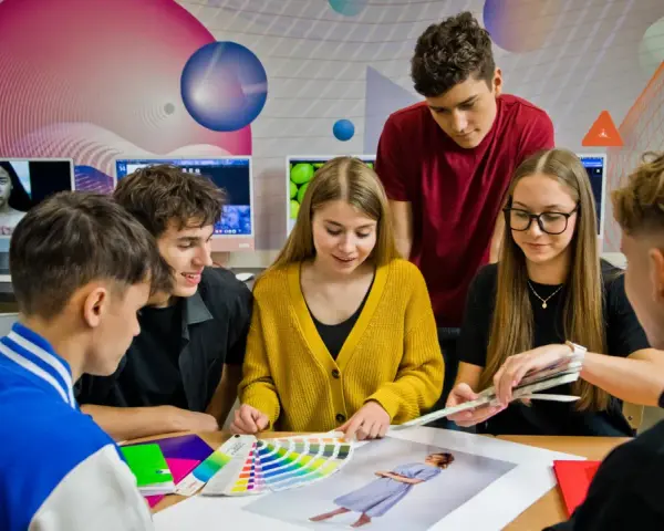 Grupa młodych ludzi dyskutuje nad próbkami kolorów i zdjęciami przy biurku.