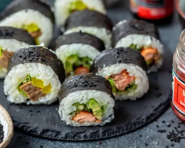 Gotowe sushi z łososiem i awokado, idealne do nauki jak zrobić sushi w domu. Obok słoiczek marynowanego imbiru.