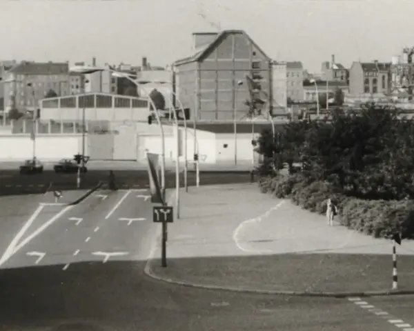 Straßenszene in Berlin der 80er Jahre mit Autos, Ampeln und einem Kran im Hintergrund.