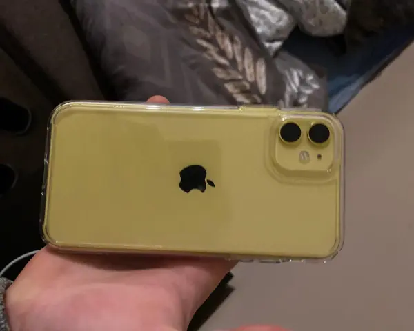 Żółty iPhone 11 w przezroczystym etui, trzymany w dłoni.