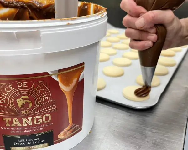 Un repostero usa una manga pastelera para decorar galletas con dulce de leche, mostrando cómo hacer dulce de leche.