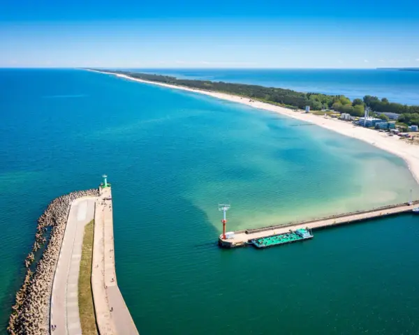 Władysławowo miasto, port z falochronem i latarnią morską, na tle piaszczystej plaży i turkusowego morza.