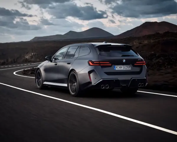 Mocne BMW M5 Touring pędzi po krętej drodze pośród surowego krajobrazu.