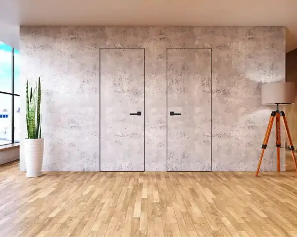 Minimalistyczne drzwi w betonowej ścianie, idealne, by zamaskować przejście. Obok stoi roślina i lampa.
