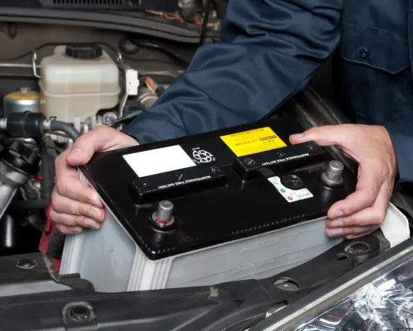 Mekaniker byter ett urladdat bilbatteri i motorutrymmet.