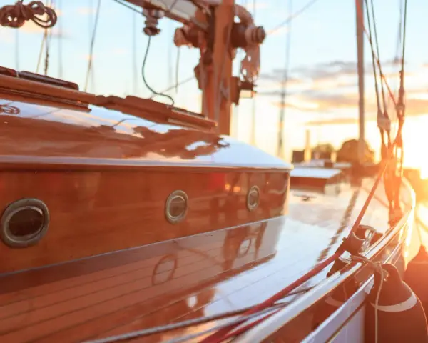 Glänzendes Holzdeck eines Segelboots, frisch lackiert. Kleine Bullaugen spiegeln die untergehende Sonne wider.