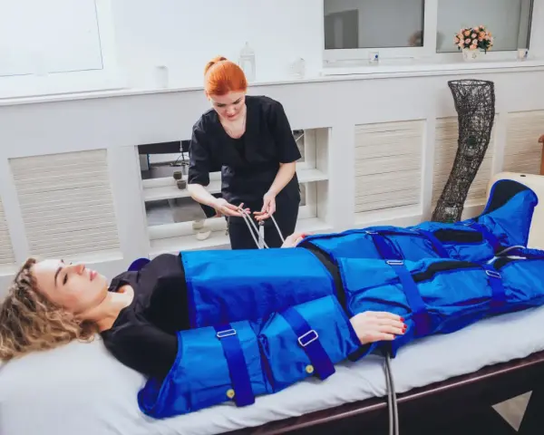 Kobieta w salonie piękności przechodzi zabieg drenażu limfatycznego. Terapeuta przygotowuje urządzenie do masażu uciskowego.
