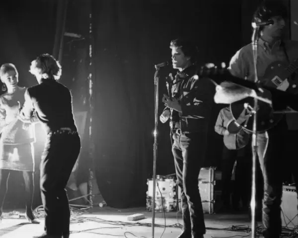 Scène de concert des membres de The Velvet Underground. Une femme danse à gauche, tandis que Lou Reed chante au micro.