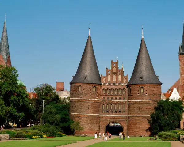 Holstentor in Lübeck, ein Wahrzeichen für Ihre **Ferien Schleswig-Holstein 2025**. Historische Backsteinarchitektur mit Türmen und grünen Parks.