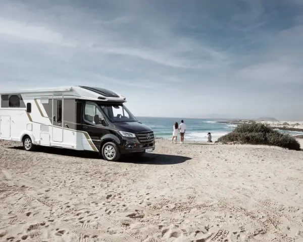 Eura Mobil husbil parkerad på en sandstrand vid havet. Ett par står och tittar ut över vågorna.