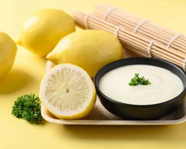 Un bol de sauce beurre citron crémeuse, garni de persil, avec des citrons frais et un rouleau de bambou en arrière-plan.