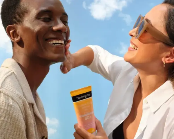 Un couple rit sous un ciel bleu, une femme appliquant une crème solaire Neutrogena. Une liste de protection contre le soleil pour une peau saine.