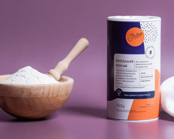Holzschale mit weißem Konjakmehl und Löffel daneben, eine Dose mit der Aufschrift "Konjakmehl" und Produktinformationen.