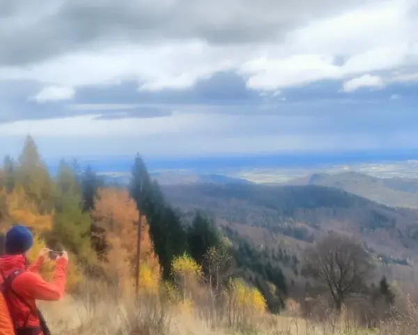 Widok na Beskid Mały jesienią. Turysta z pomarańczowym plecakiem fotografuje panoramę.