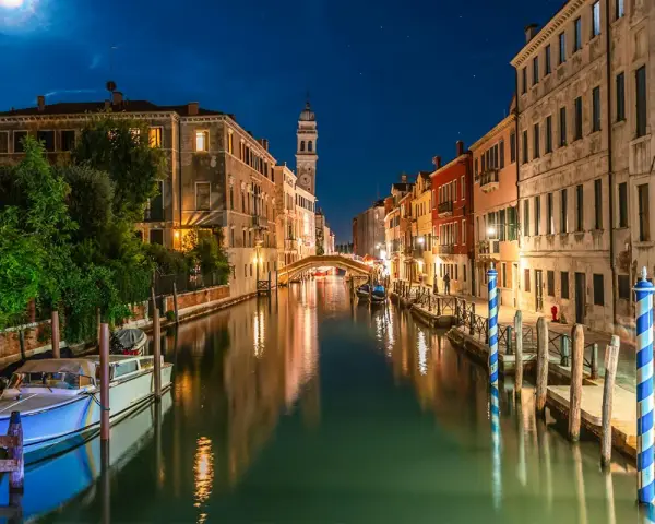 Una gondola venezia di notte, con luci soffuse che si riflettono sull'acqua e un cielo stellato.