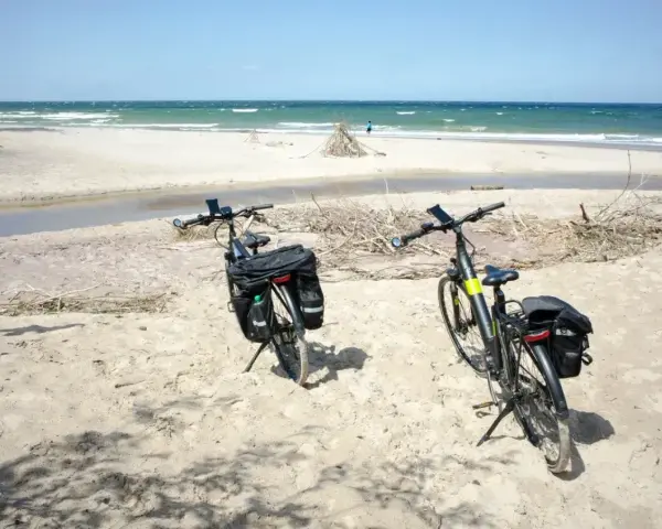 Dwa rowery z sakwami na piaszczystej plaży, gotowe na odkrywanie tras rowerowych nad morzem.