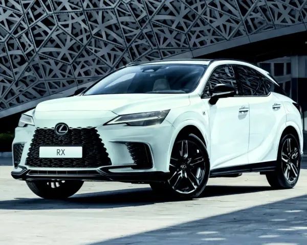 Biały Lexus RX500h z czarnymi felgami stoi przed nowoczesnym budynkiem o geometrycznej fasadzie.