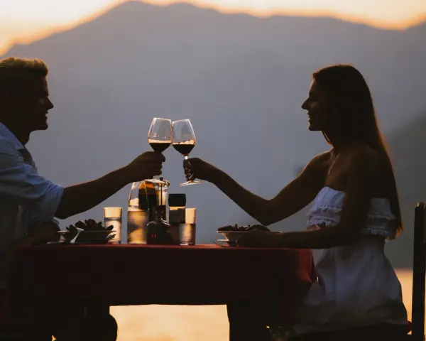 Idealne miejsce na pierwszą randkę: para wznosi toast winem przy romantycznej kolacji na tle zachodzącego słońca i gór.