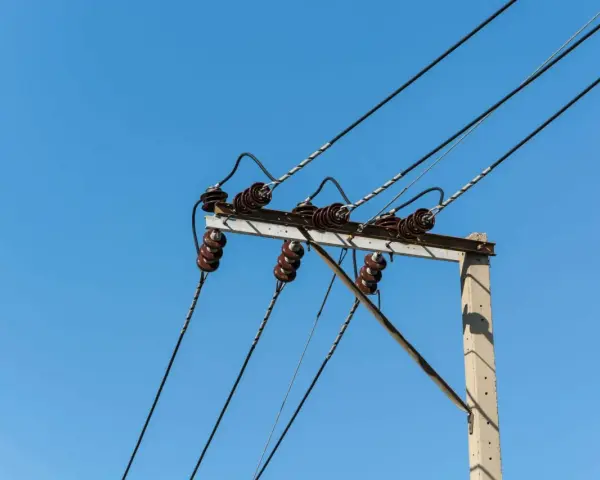Słupy energetyczne z izolatorami ceramicznymi i przewodami pod napięciem. Brak zgody na służebność przesyłu może oznaczać problemy z infrastrukturą.