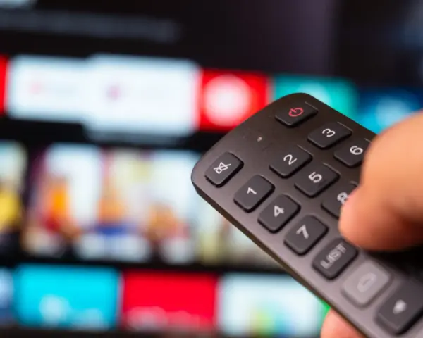 Dłoń trzyma pilot do telewizora, wybierając film na ekranie. To idealny moment na relaks z web tv.