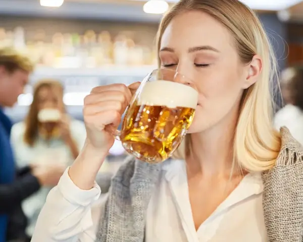 Kobieta z zamkniętymi oczami pije piwo bezalkoholowe w ciąży, ciesząc się smakiem w pubie.