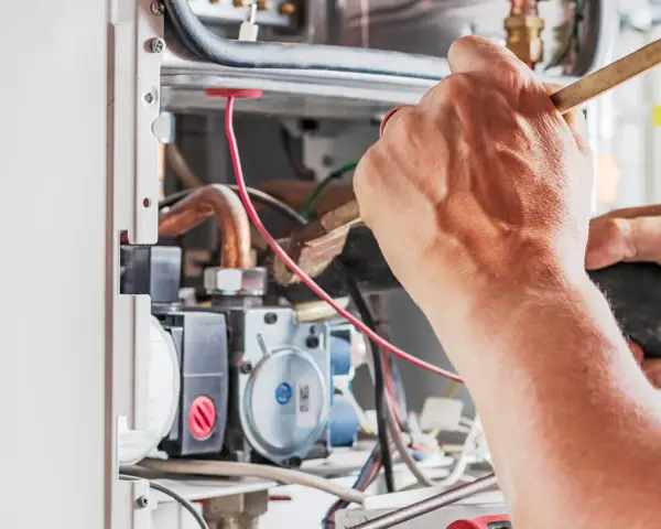 Tecnico che lavora su un **scambiatore acqua calda**, pulendo componenti interni con un pennello e un aspiratore.
