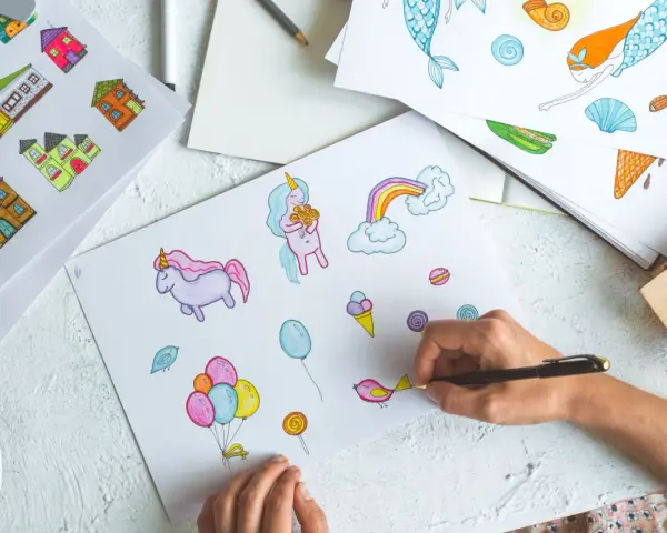 Une main dessine des licornes, des maisons et des bonbons, une scène parfaite pour une formation illustrateur jeunesse.