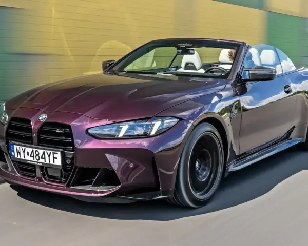 Fioletowe BMW M4 Competition kabriolet pędzi po drodze, odsłaniając białe wnętrze i sportowe detale.