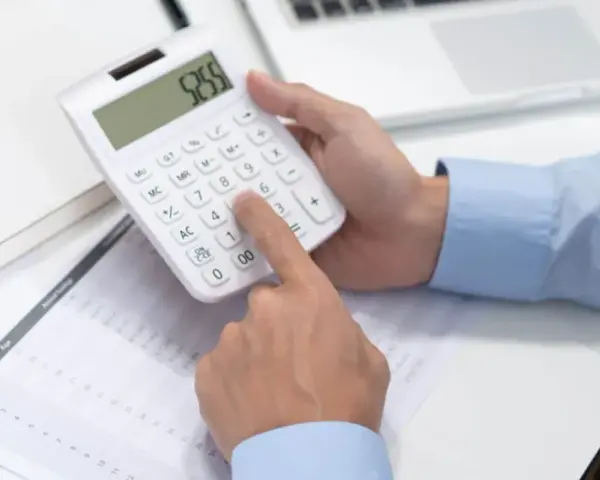 Persona calculando en calculadora blanca, revisando documentos y tablet. Se pregunta cuánto cuesta abrir una empresa en España.